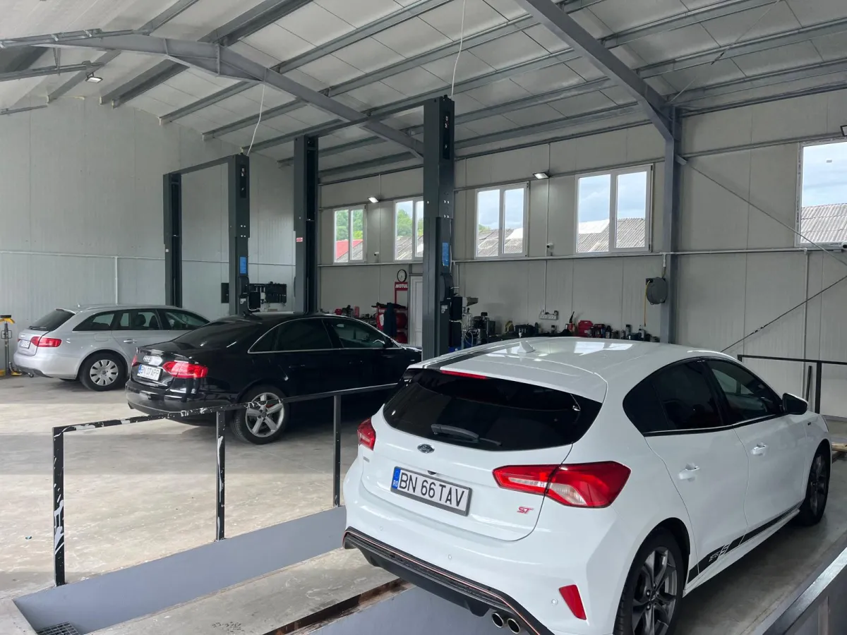 Hală de service bine organizată, cu vehicule pe standuri și zonă dedicată lucrărilor mecanice.